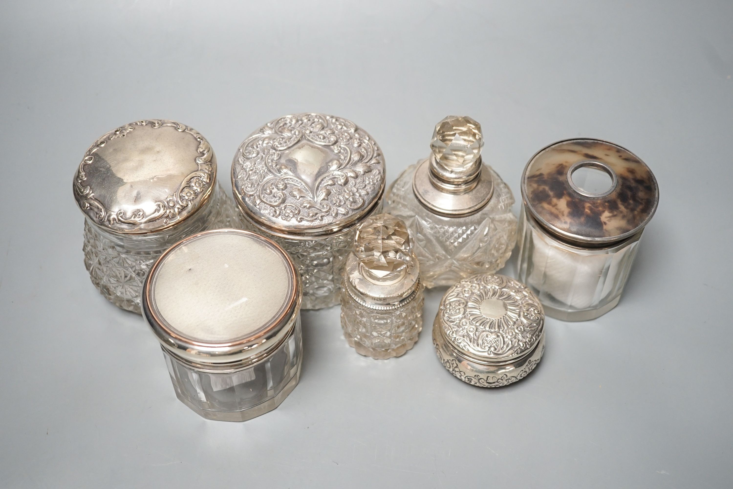 A circular embossed silver box and six silver mounted glass toilet bottles.